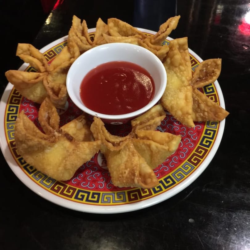 Crispy crab rangoon appetizers arranged around a small bowl of sweet and sour sauce on a decorative plate.
