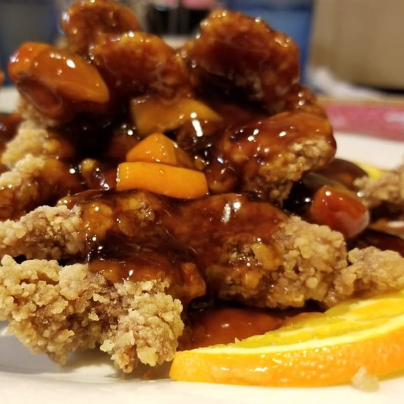 Crispy orange chicken with a glossy sauce and orange slices on a white plate at Bao Bao Chinese Bistro.