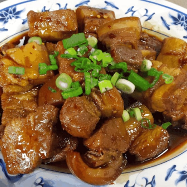 Braised pork belly with potatoes and green onions in a rich sauce on a white and blue plate.