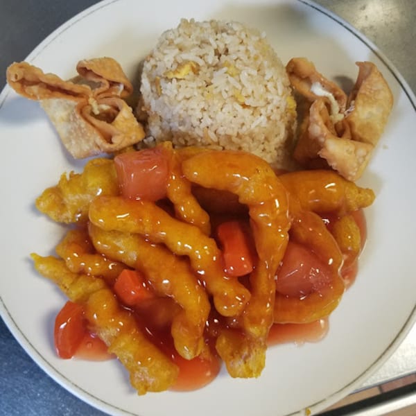 Sweet and sour chicken with fried rice and two crab rangoons on a white plate.